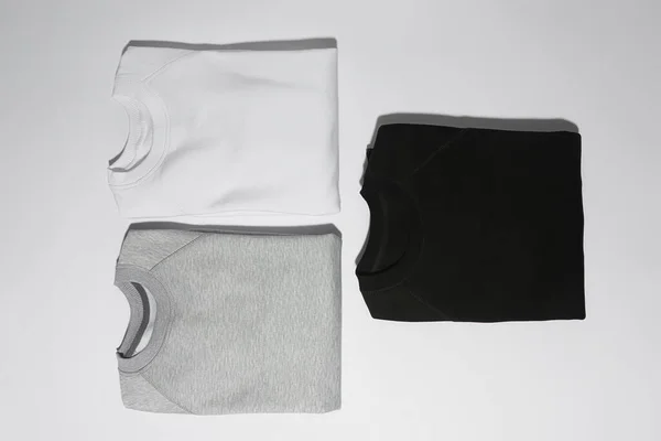 평평하게 접혀 있는 세 개의 완벽하게 접혀 있는 단색 스웨터 회색, 검은색 과 흰색 이 흰색 배경 위로 분리되어 있다 — 스톡 사진