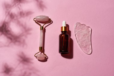 Gül kuvars taşının üst görüntüsü, yeşil silindir ve pembe yüzeyde izole edilmiş cam göz damlası serumu şişesi.