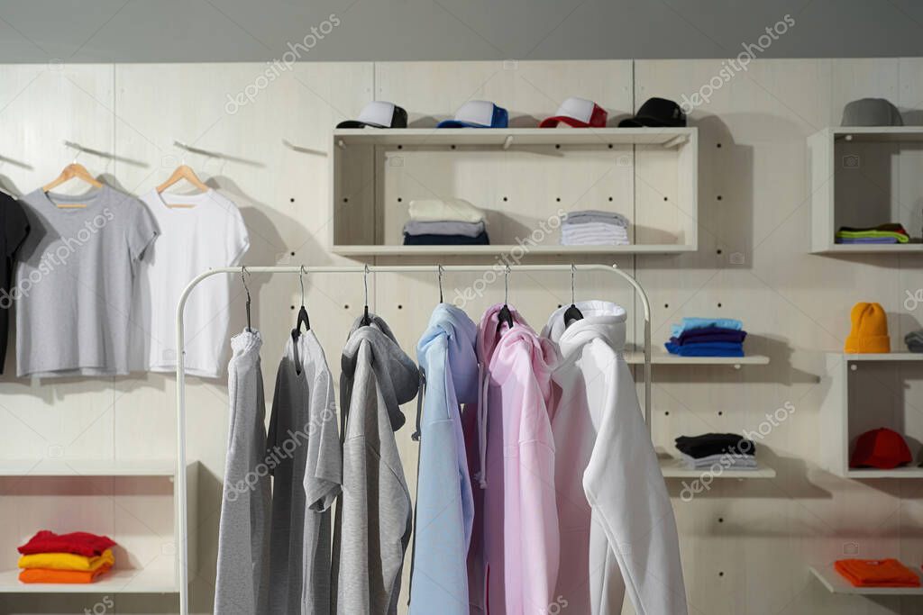 Clothes at custom clothing printing company. Set of blank pastel cotton white, gray, blue and pink sportswear on a rail in the store. Horizontal shot