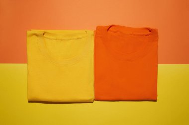 İki katlanmış sarı ve turuncu pamuklu tişört yaratıcı renkli arka planda izole edilmiş. Düz yatay tişört şablonu