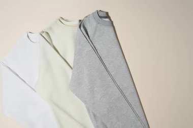 Katlanmış gri, beyaz ve fildişi renkli spor kazaklar soluk bej arka planda izole edilmiş.