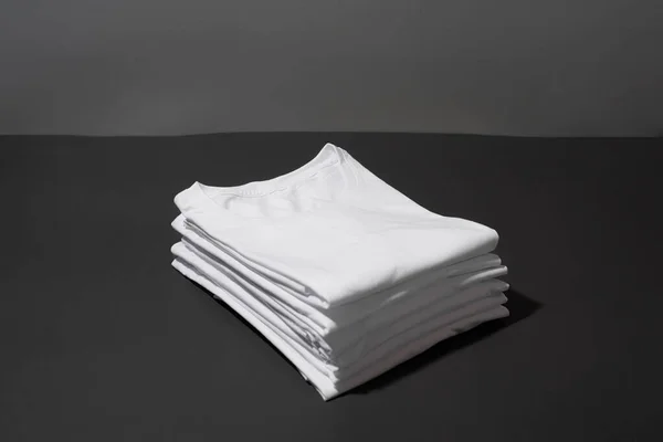 하얀 면 셔츠가 쌓여 있는 것을 클로즈업 한 어두운 회색 배경 위로 분리되어 있다 — 스톡 사진