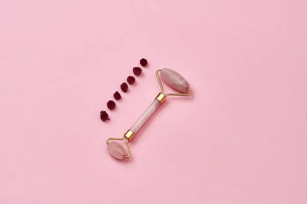 Colocação plana de rosa de quartzo rolo de massagem facial e botões de rosa secas isoladas sobre fundo rosa — Fotografia de Stock