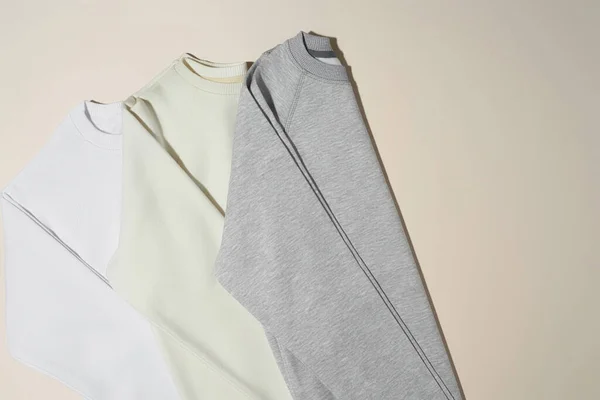 Pose écaille de sweat-shirts sport blancs, gris et ivoire pliés isolés sur fond beige pâle — Photo