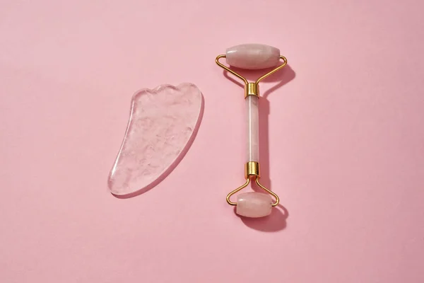 Ferramentas de massagem facial de quartzo rosa, rolo facial e raspador Gua Sha isolado sobre fundo rosa — Fotografia de Stock