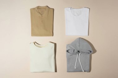 Pastel yığını mükemmel katlanmış pamuk polo, tişört, kapüşon ve tişört soluk bej arka planda izole edilmiş.