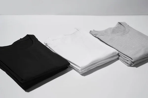 Drei gefaltete einfarbige T-Shirts grau, schwarz und weiß isoliert über grauem Hintergrund — Stockfoto