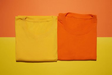 İki katlanmış sarı ve turuncu pamuklu tişört yaratıcı renkli arka planda izole edilmiş. Düz yatay tişört şablonu