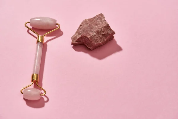 Pedra áspera de quartzo rosa cru natural e rolo de massagem facial isolado sobre fundo rosa — Fotografia de Stock
