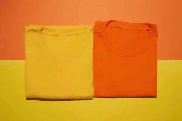 Two folded yellow and orange cotton t shirts isolated on creative colorful background. Flat lay tees template — Stock Photo, Image