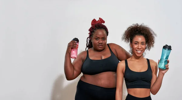 Dos mujeres afro vestidas con ropa deportiva y sosteniendo botellas — Foto de Stock