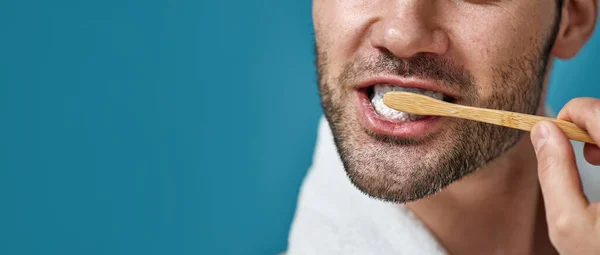 Gehakt schot van de mens met handdoek rond zijn nek poetsen zijn tanden geïsoleerd over blauwe achtergrond — Stockfoto