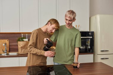 Neşeli homoseksüel çift fincanlara kahve dolduruyor.