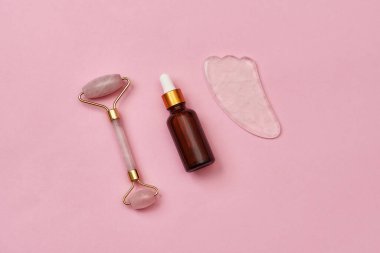 Gül kuvars yşa taşı, yeşim silindir ve pembe yüzeyde izole edilmiş cam göz damlası serumu şişesi.