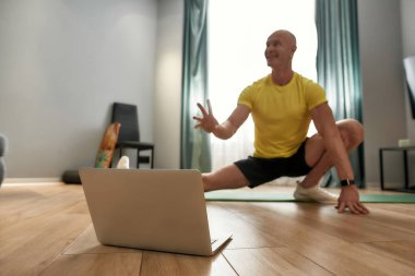 Kendini izole ederken aktif kal. Evde çevrimiçi eğitim yaparken spor giyimi antrenörlüğü yapan ve dizüstü bilgisayara bakan olgun bir kişisel antrenör.