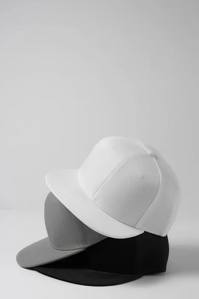 Closeup shot of three blank monochrome white, gray and black baseball cap isolated over light background — Stock Photo, Image