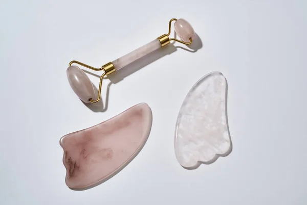 Ferramentas de massagem facial de quartzo rosa, rolo de rosto e raspadores Gua Sha isolados em fundo claro — Fotografia de Stock