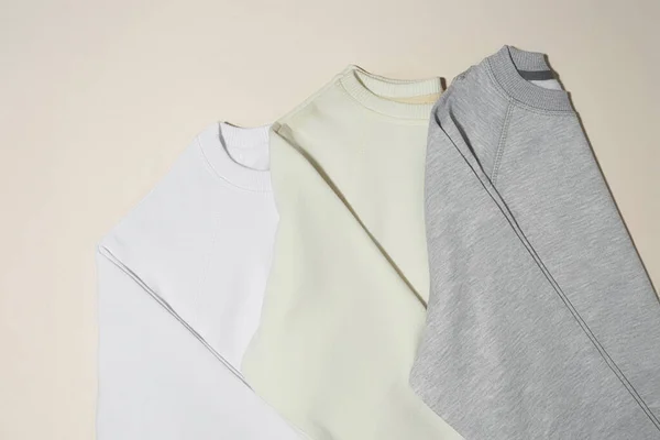 Gros plan de sweat-shirts sport blancs, gris et ivoire pliés isolés sur fond beige pâle — Photo