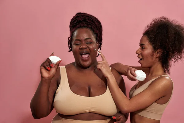 Pareja de mujeres jóvenes divirtiéndose con crema cosmética — Foto de Stock