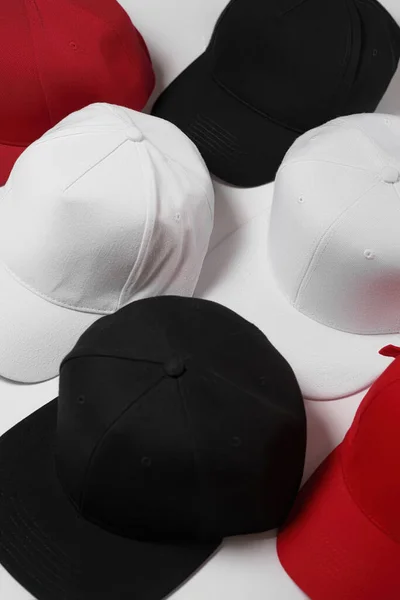 검은 색, 흰색, 빨간색의 야구 스냅 백 모자 세트가 흰 표면 위에 놓여져 있다 — 스톡 사진
