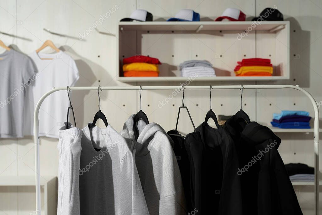 Clothes at custom clothing printing company. Set of blank monochrome cotton white, gray, black sportswear on a rail in the store. Horizontal shot