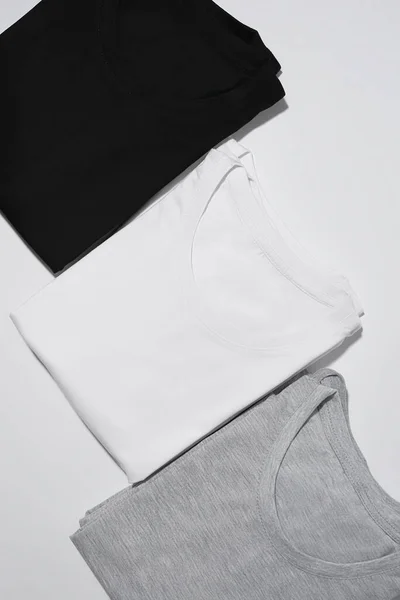 Três camisetas monocromáticas dobradas cinza, preto e branco isolado sobre fundo cinza — Fotografia de Stock