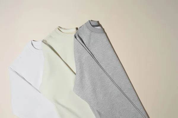 Sweats sport blancs, gris et ivoire pliés isolés sur fond beige pâle — Photo