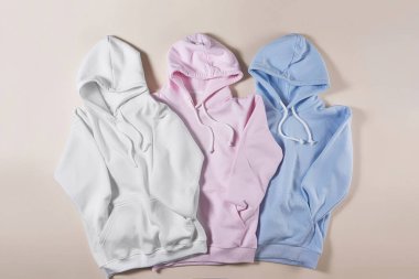 Üç beyaz, mavi ve pembe pastel boş pamuklu kapüşonlu soluk bej arka planda yalıtılmış.