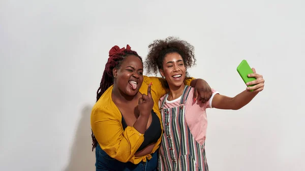 Dos mujeres afro están haciendo una selfie en un teléfono inteligente verde — Foto de Stock