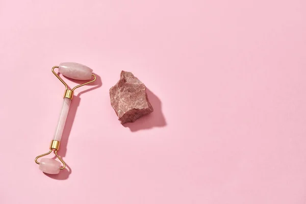 Rolo de massagem facial de quartzo rosa e pedra áspera crua natural isolada sobre fundo rosa — Fotografia de Stock