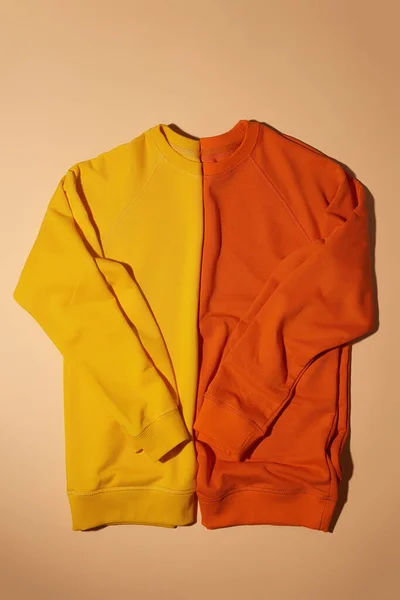 Top view of two folded yellow and orange sport sweatshirts lying vertically isolated on light beige background — Stock Photo, Image