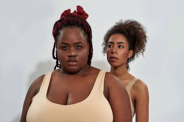 Portrait of plus size african american woman in underwear looking at camera, standing together with slim friend isolated over gray background — Stock Photo, Image