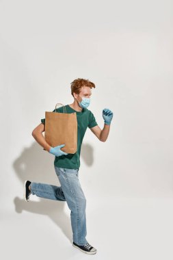 Kafkasyalı genç kurye koşarken elinde kağıt paketi tutuyor.