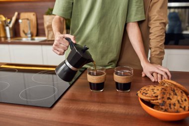 Genç eşcinsel çift fincanlara kahve dolduruyor.