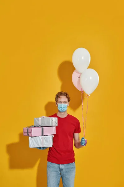Mensajero en máscara y guantes sosteniendo regalos y globos —  Fotos de Stock