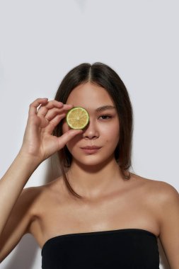 Gözünün yanında limon dilimi tutan mutlu Asyalı kız.