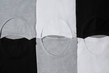 Top view of folded monochrome cotton t shirts of black, gray and white colors clipart