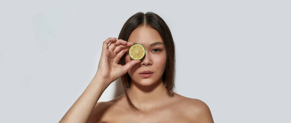 Young asian girl holding lime slice near her eye