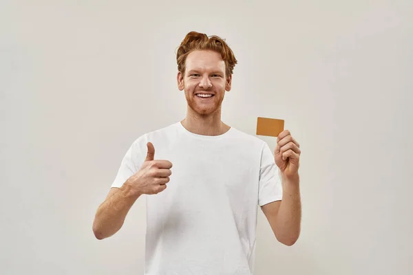 젊은 빨간 머리 남자 손에 신용 카드를 들고 엄지 손가락을 보여 줍니다. — 스톡 사진
