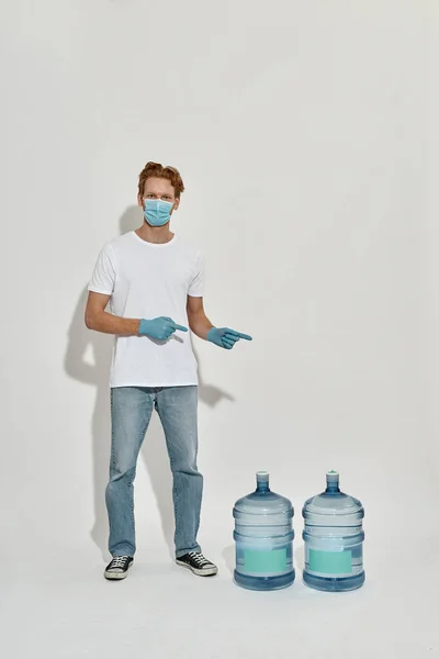 Young redhead guy pointing at huge bottles of the water — Stock Photo, Image