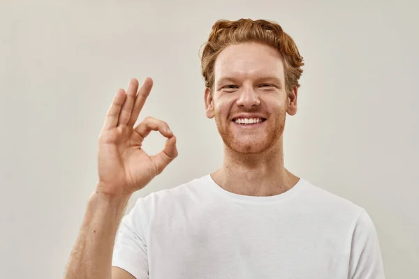 Jongeman staat voor de grijze muur en toont ok met de hand — Stockfoto