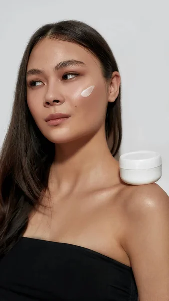 Молодая азиатка с мазком крема для лица на щеке — стоковое фото