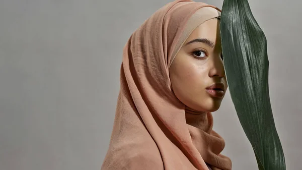Giovane donna araba in hijab accanto alla foglia verde — Foto Stock