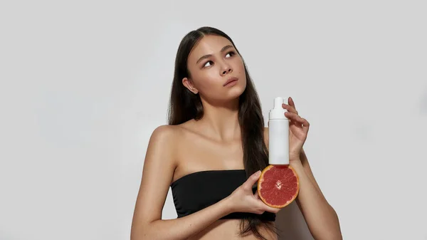 Joven mujer asiática sosteniendo pomelo y producto cosmetológico — Foto de Stock