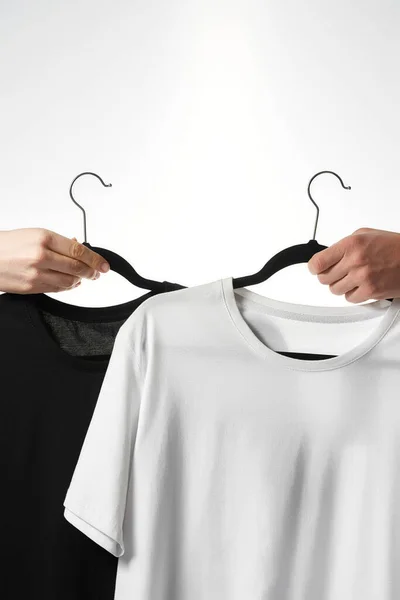 Gri arkaplana karşı askılarda siyah ve beyaz temel tişörtler — Stok fotoğraf