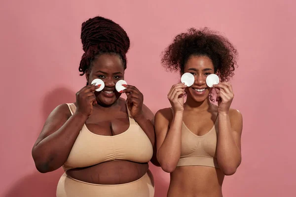 Pár ženských afro přátel v béžovém spodním prádle s bavlněnými houbami — Stock fotografie