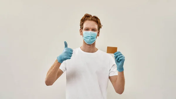 Young redhead courier shows thumb up and holds a credit card — Stock Photo, Image