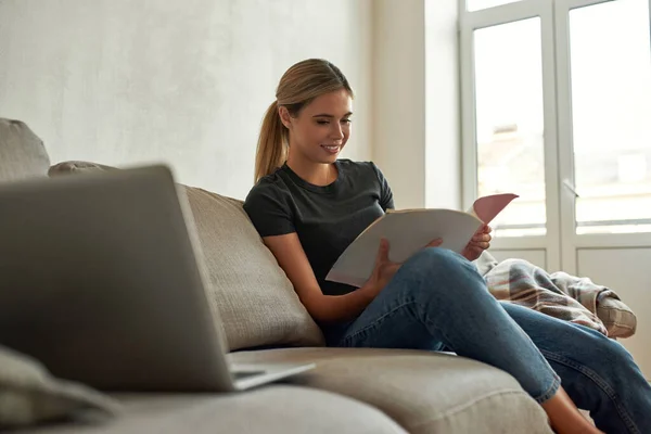 Jovem mulher lê documentos enquanto se senta no sofá — Fotografia de Stock