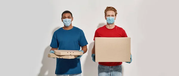 Smíšené závodní kurýři v rukavicích a maskách drží krabice — Stock fotografie