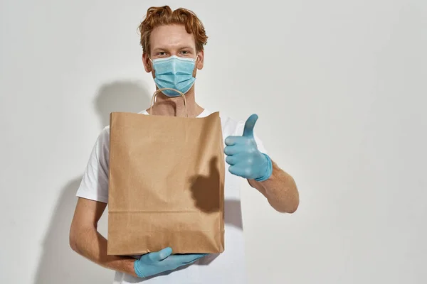 Picture of a young redhead courier holding paper bag and thumb up — Stock Photo, Image